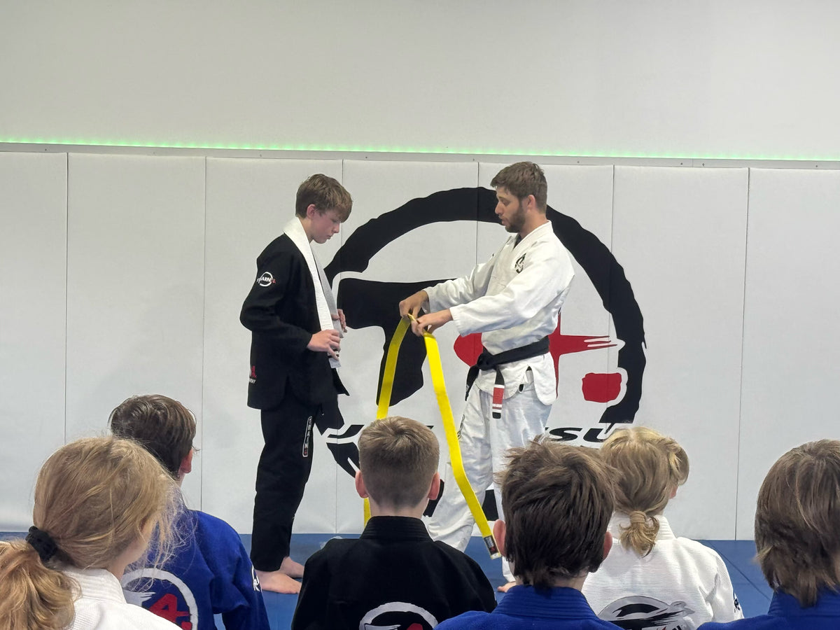 A Train4 coach presenting a belt to a child while the kids class watches